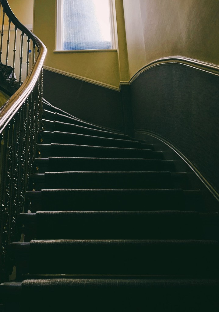 An old-fashioned staircase, with carpet, curving upwards.